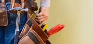 Person wearing a tool belt with a hammer, pliers, and other tools visible.